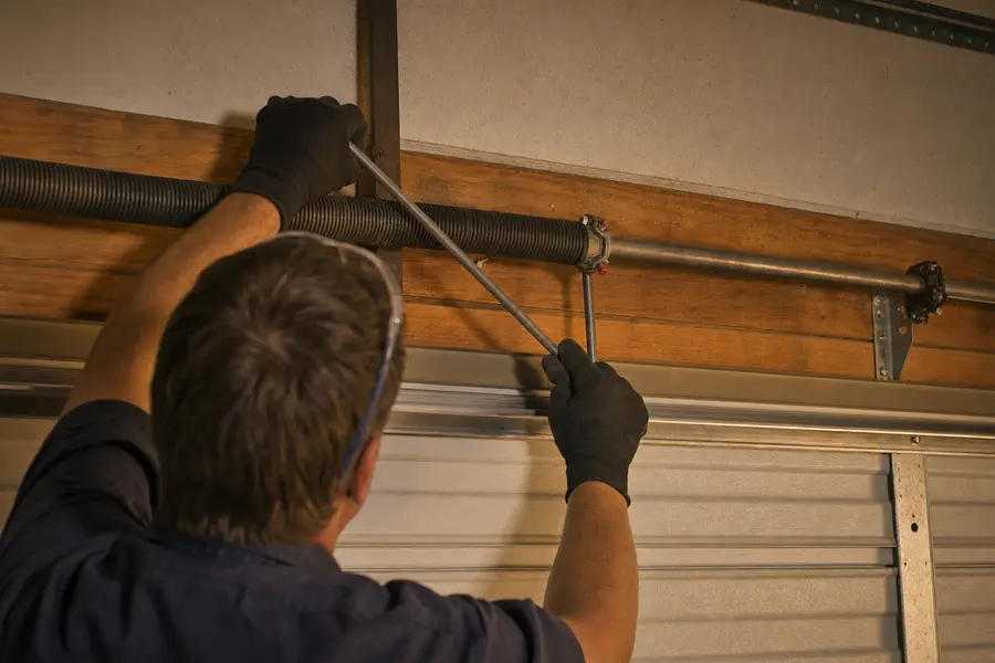 Technician fitting winding bars to a torsion spring above a closed garage door